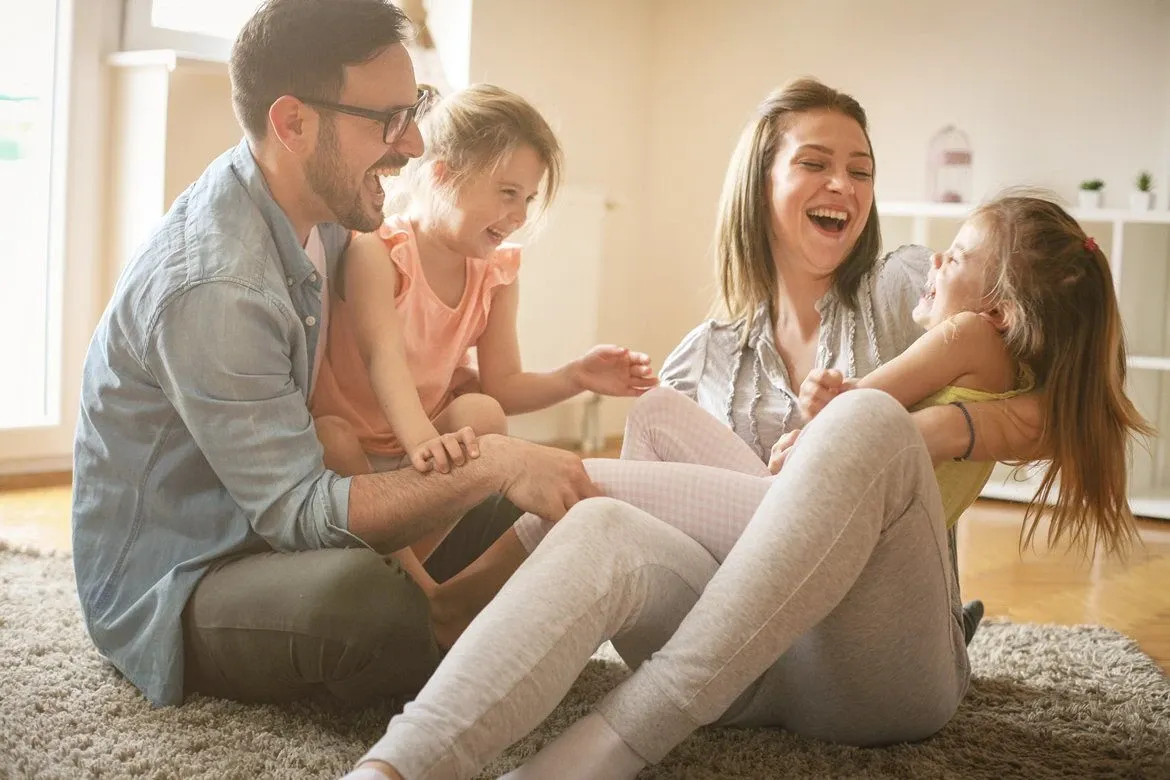 A smiling family of four hugging outdoors on a sunny day